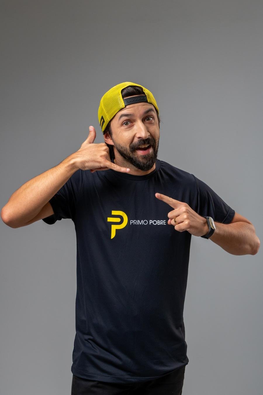 Primo Pobre fazendo sinal de “me liga” e apontando para o logo na camiseta