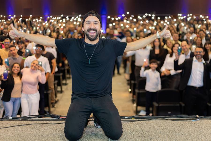 Primo Pobre ajoelhado no palco do Sebrae Minas com a plateia acendendo as lanternas dos celulares
